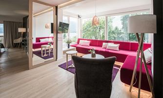 A modern living room with a red sofa and large windows. The decor is bright and inviting, with a cozy table and stylish lamps.