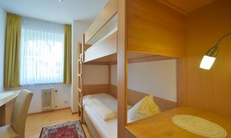A simple room with a bunk bed and a desk. Bright curtains create a friendly atmosphere.