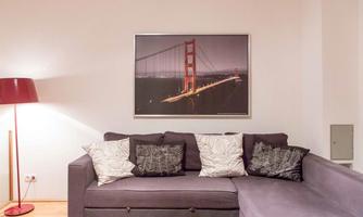 A cozy living room with a gray sofa and cushions. A picture of the Golden Gate Bridge hangs on the wall.