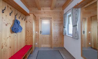 A cozy hallway with wooden paneling and a red bench. Coat hooks hang on the wall and a mirror reflects the space.