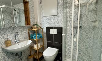 A modern bathroom with a shower, a sink, and a toilet. The walls are decorated with tiles and there are towels in various colors.