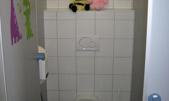 A small bathroom with a toilet in the middle. Above are two plush toys and colorful wall stickers decorate the walls.