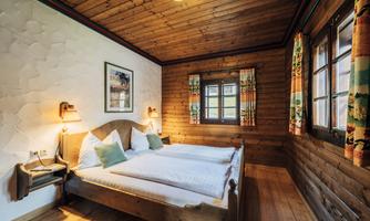 A cozy bedroom with wooden walls and a double bed. The room features windows with colorful curtains and soft lighting.