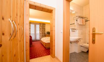 A bright hallway that leads to a bedroom and a bathroom. The bedroom is equipped with a double bed and a television.