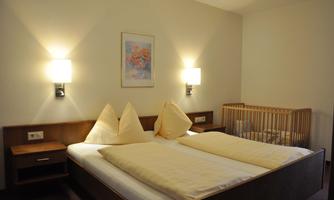A cozy hotel room with a double bed and two pillows. In the background, there is a crib.