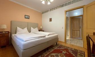 A cozy bedroom with a large double bed and softly padded pillows. The walls are painted in gentle colors and there is a beautiful carpet on the floor.