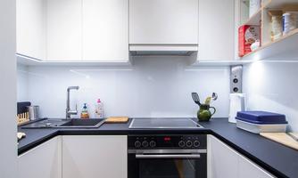 A modern kitchen with white furniture and a dark countertop. It is well-lit and displays a clean, organized space.
