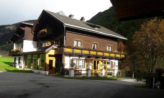 A traditional alpine house with wooden siding and colorful windows. In the background, mountains and trees can be seen.
