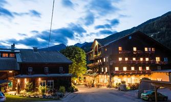 A cozy inn and a traditional building at dusk. The warm lights create an inviting atmosphere in front of a beautiful mountain landscape.