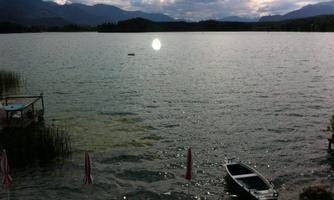 A serene lake with a boat and a relaxing atmosphere. In the background, gentle mountains and a cloudy sky are visible.