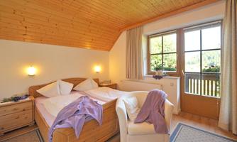 A cozy bedroom with a double bed and a seating area. Large windows offer a view of the outdoors and let in plenty of light.