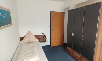A simple bedroom with a single bed and a large wardrobe. The room has carpet flooring and a desk next to the bed.