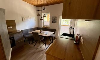 A modern kitchen with a dining table and chairs. The walls are light, and there are wooden details in the ceiling and furniture.