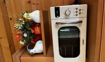 A modern microwave stands on a kitchen countertop. Above it are colorful flowers and decorative jugs.