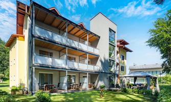 A pretty yellow hotel with many windows and balconies. The garden is green and inviting, ideal for guests to relax.