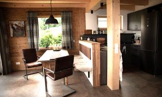 A modern kitchen with a dining area in a wooden house. Natural light falls on the table and chairs through the window.