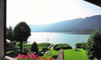 A quiet lake with gentle hills in the background. Colorful flowers and a green meadow line the shore.