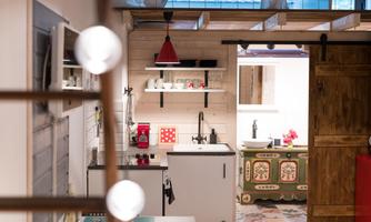 A modern kitchen unit with a red lamp and various kitchen appliances. The room has a rustic character with a wooden cabinet in the background.