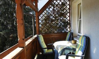 A cozy balcony with wooden paneling and a table. Two chairs with colorful cushions invite you to relax.