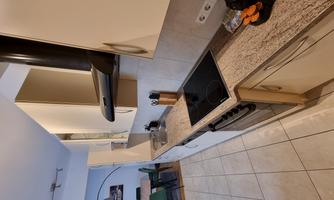 A modern kitchen with bright cabinets and a granite surface. In the background, a dining table and chairs are visible.