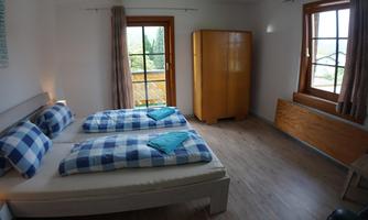 A simple bedroom with two single beds and checkered design pillows. The room has large windows that let in plenty of light.