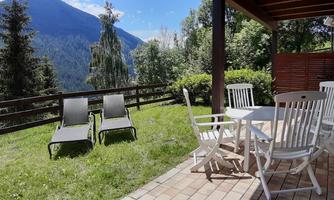 A cozy outdoor area with lounges and a dining table. In the background, mountains and green spaces can be seen.