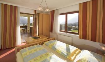 A cozy bedroom with two beds and colorful curtains. Through the windows, there is a beautiful view of the landscape.