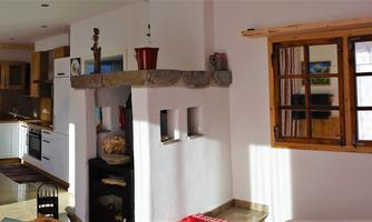 A cozy living space with wooden details and a large window. The room is bright and inviting with an open kitchen area.