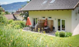 A cozy house with a terrace and orange sunshades. The garden is surrounded by colorful flowers and green meadows.