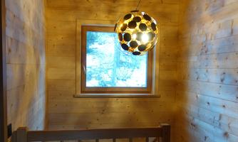 A bright hallway with wooden paneling. A creative lamp hangs over the stair area next to a window with a view to the outside.