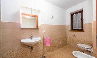 A modern bathroom with bright tiles and a large mirror. There is a sink, a toilet, and a towel rack with a pink towel.