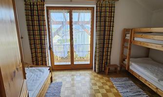 A bright bedroom with a bunk bed and a single bed. Large windows with an outside view let in plenty of light.