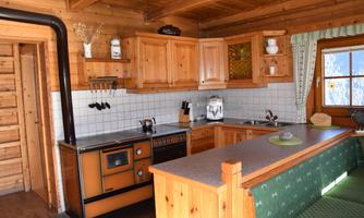 A cozy kitchen in a log cabin with modern appliances. The furnishings are made of wood, and there is plenty of daylight through the window.