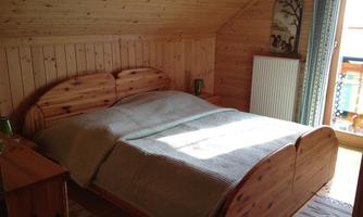A cozy bedroom with a large wooden bed and a warm, wood-paneled ambiance. The light falls gently through a window, creating an inviting atmosphere.
