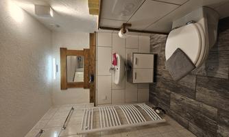 A modern bathroom with neutral tiles and bright light. It includes a sink, a toilet, and some towels.