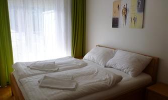 A cozy bedroom with a double bed and fresh bedding. The windows are decorated with light curtains and green drapes.