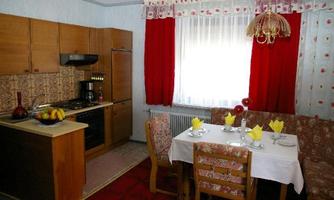 A cozy kitchen with a dining table set for four people. The walls are designed in a soft blue with red curtains and wooden cabinets.