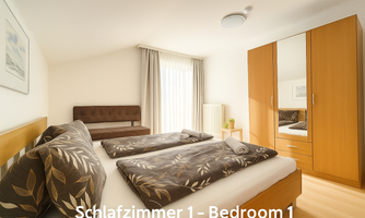 A cozy bedroom with a double bed and an adjacent sofa bed. A large wardrobe and windows with curtains provide plenty of light.