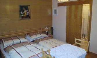 A cozy bedroom with a double bed, bright bed linens, and a small table. A piece of art hangs on the wall and the furniture is made of wood.
