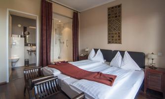 A cozy bedroom with two single beds and modern furniture. In the background, a bathroom with a shower can be seen.
