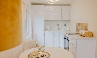 A modern kitchen with white cabinets and stainless steel appliances. On the table, there is a coffee cup and some sweets placed.