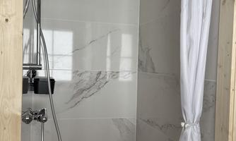 A modern shower with smooth tiles and a white shower curtain. The shower is well-lit and features a simple, elegant design.