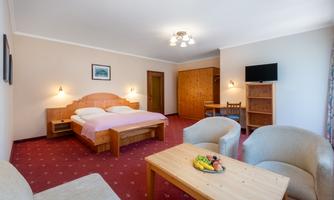 A cozy room with a double bed, a table, and two armchairs. There is a television and wooden cabinets that create a warm atmosphere.