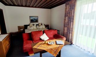 A cozy living space with a red sofa and a wooden table.  
Spacious windows let in plenty of daylight and offer a view of the greenery outside.