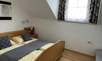A cozy bedroom with a double bed and yellow pillows. A window with curtains lets in natural light.
