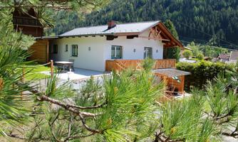 A modern house surrounded by green trees and mountains. The terrace and the garden invite you to relax.