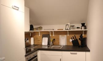 A modern kitchen with white cabinets and a wooden shelf. Kitchen utensils and appliances are on the countertop.