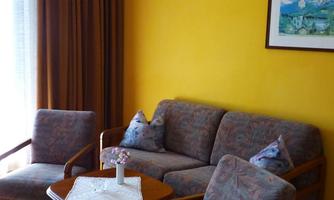 A cozy living area with a beige couch and two armchairs. The wall is painted in a warm yellow tone and there are curtains as well as a piece of artwork.