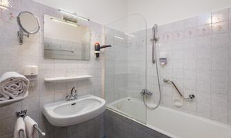 A modern bathroom with a bathtub and a shower combination. There is a sink, a mirror, and fresh towels.