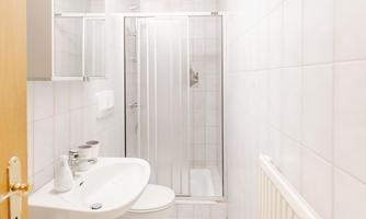 A small bathroom with white tiles. There is a shower, a sink, and a toilet.